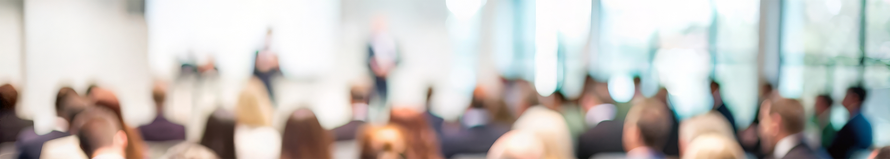 A conference audience listens to a presentation onstage | Adobe Stock